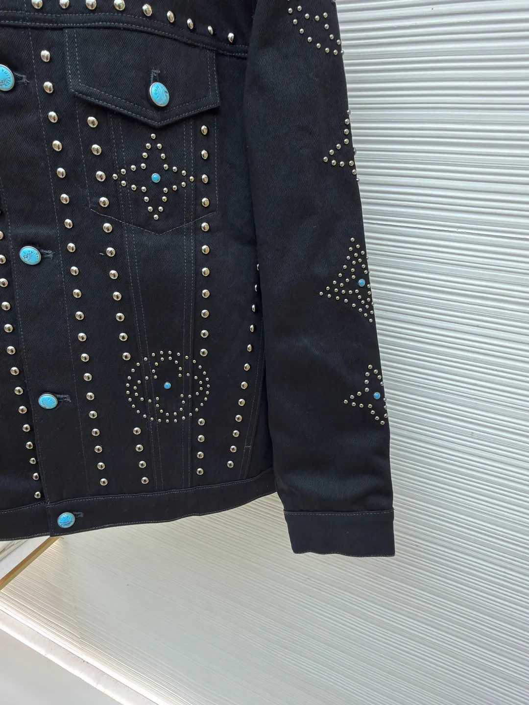 LOUIS VUITTON turquoise rivet denim jacket ●Original version: purchased and developed by 38979 ●Item number: 1682224-E30 ●Material: denim fabric ●Technology: hand-made rivet inlay ●Color: black ●Version: fitted version ●Weight: about 1550 grams ●Size: 46-48-50-52 ●Description: This black denim jacket is made of high-density twill denim fabric and has been treated with pre-washing water. It not only retains the crisp texture of the fabric, but also achieves a soft and skin-friendly wearing experience. The entire body of the garment is made of hand-made rivet inlay technology. The metal rivets are arranged at precise points to outline the outline of the brand's classic logo. Each rivet is manually hammered and fixed to ensure firmness and three-dimensionality. The placket and pockets are decorated with turquoise-textured resin buttons, which contrast with the metal rivets. The stitching on the collar, cuffs and hem adopts a double stitching process to enhance structural stability, while the edges are roughened to add a retro texture. The overall cut is a slightly loose Oversize version, combined with the three-dimensional tailoring process of the three-dimensional shoulder line, taking into account both styling and wearing comfort. Every detail is calibrated by hand, demonstrating the exquisite level of clothing making technology. The overall wiring is straight and delicate, the fabric is comfortable and soft, and the color is consistent without color difference. It can be matched with the same style to create a fashionable look and control various occasions. Customized accessories, complete with three standards, same style for men and women!